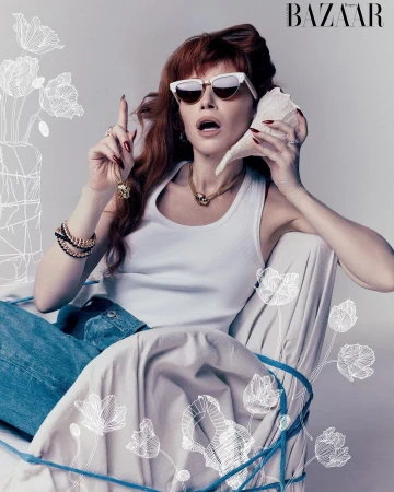 Red-haired woman in white tank top holding seashell to ear against grey backdrop with white floral illustrations.