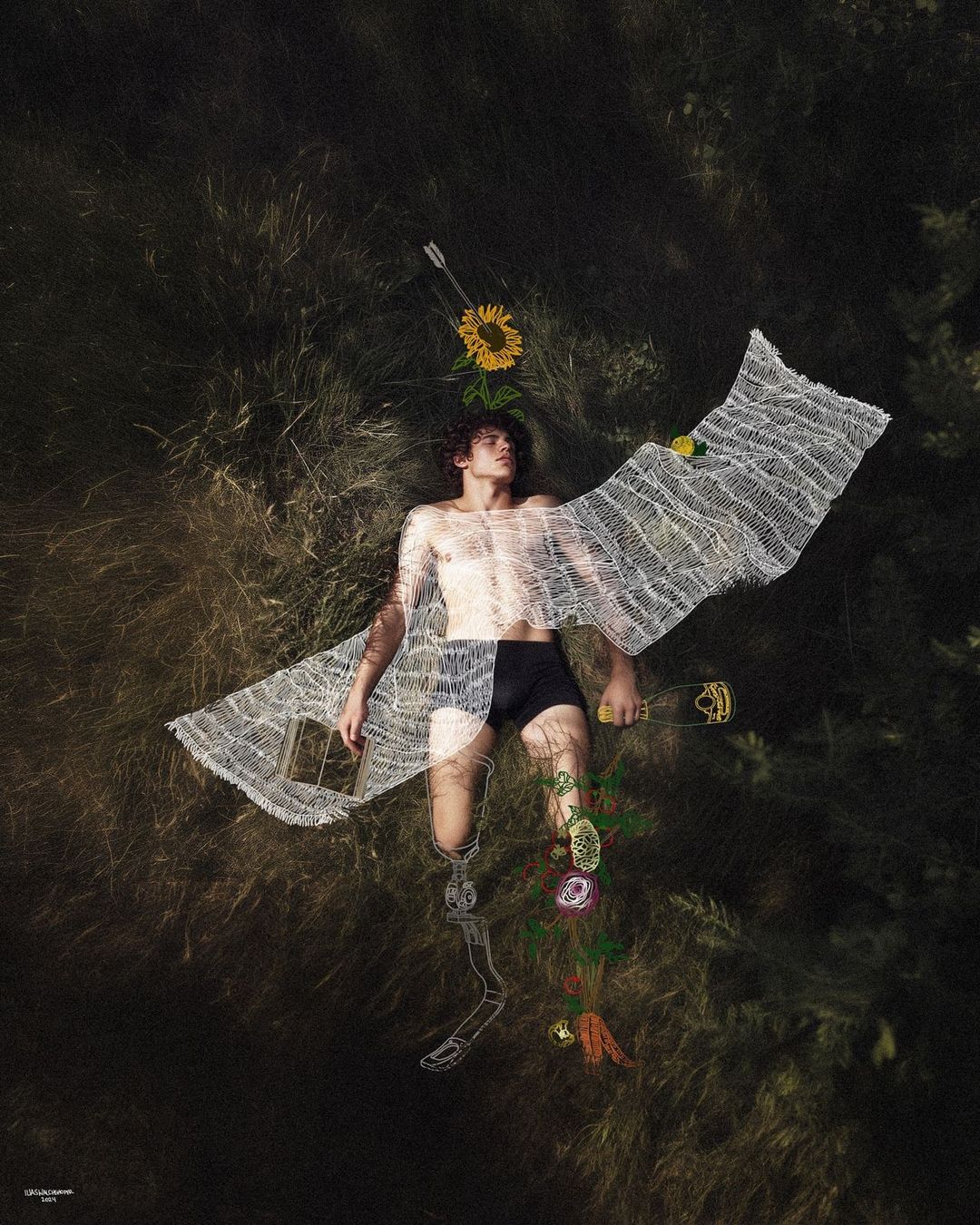 Artistic image of a young man lying in tall grass, wearing a partially sheer top with drawings of flowers and an exoskeleton on the lower half.