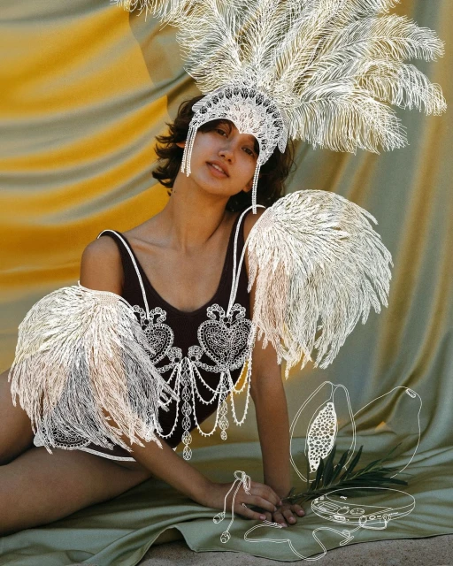 Woman in embellished leotard and feather headdress poses against draped fabric, incorporating graphic art elements and soft lighting.