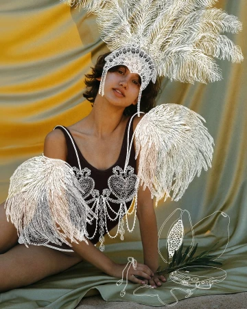 Woman in embellished leotard and feather headdress poses against draped fabric, incorporating graphic art elements and soft lighting.