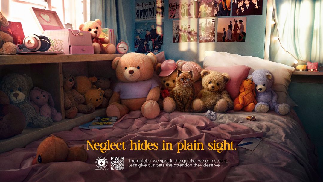 Teddy bears and a cat sit on a bed with pink bedding and posters on the wall in this colorful promotional image.