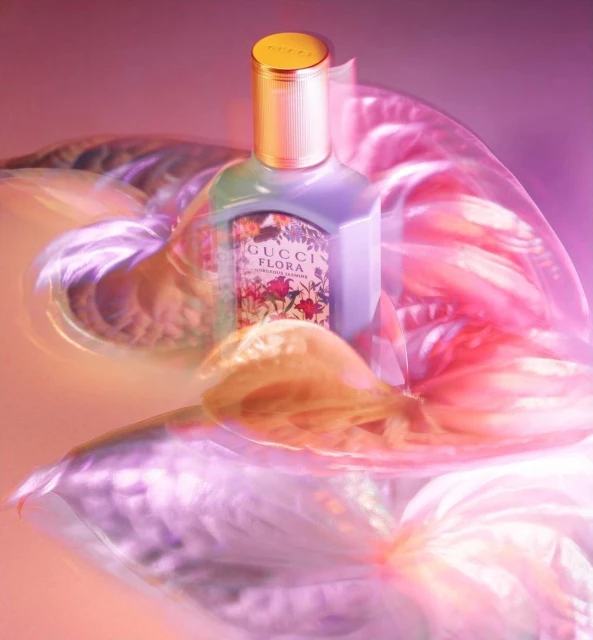 Gucci Flora perfume bottle with gold lid on a pink surface with a blurred floral background, creating a luxurious and soft aesthetic.