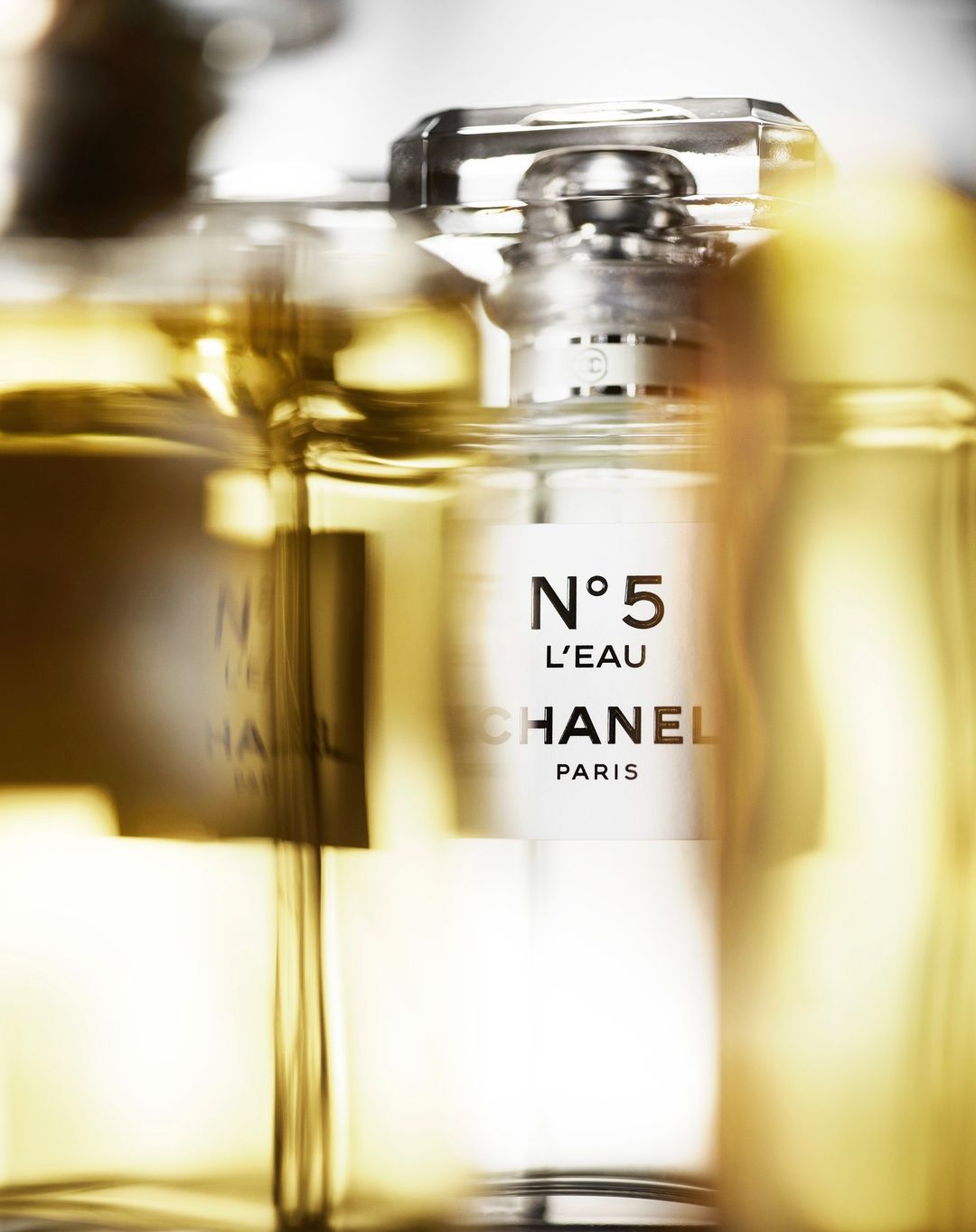Close-up of multiple Chanel No. 5 L'EAU perfume bottles, showing the glass containers and product labels with a blurred effect.