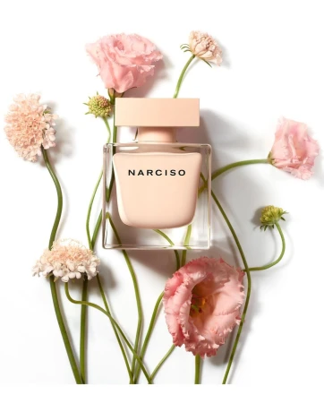 Square product photography of a glass perfume bottle surrounded by pink flowers on a seamless white background.