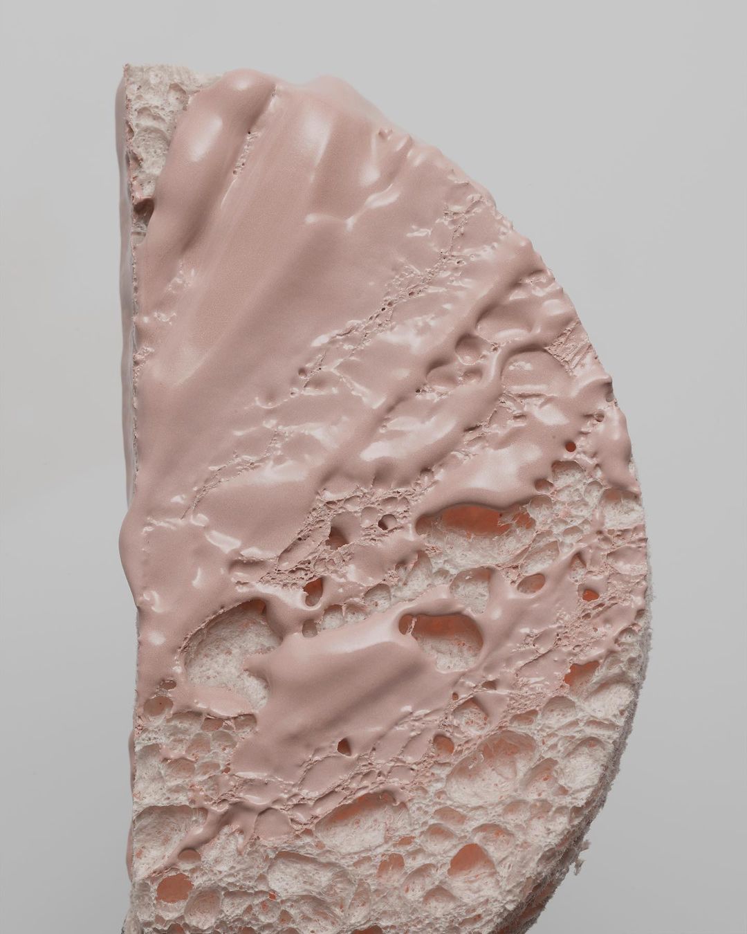 Macro shot of a half-round sponge covered in pink cream, showcasing textures and details against a neutral background.