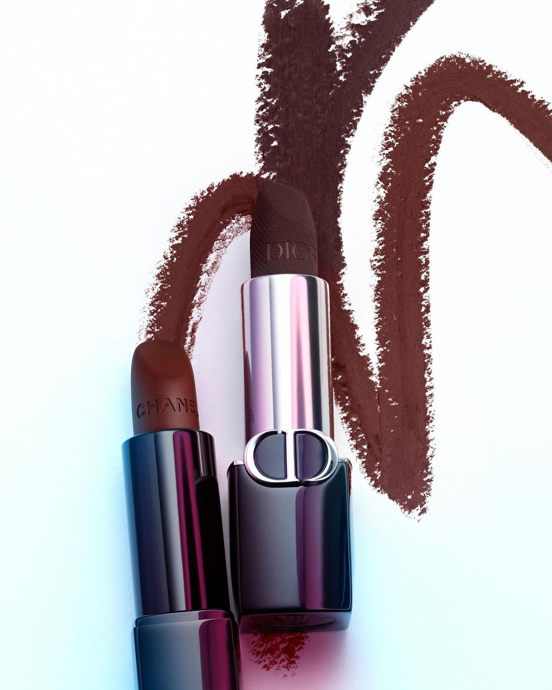Close-up studio shot of Chanel and Dior lipsticks with brown smears on a white surface, showcasing high-end beauty and fashion products.