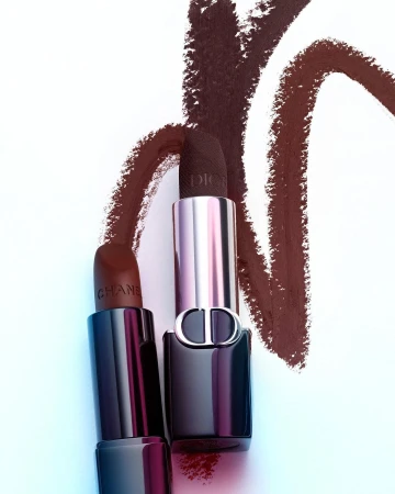 Close-up studio shot of Chanel and Dior lipsticks with brown smears on a white surface, showcasing high-end beauty and fashion products.