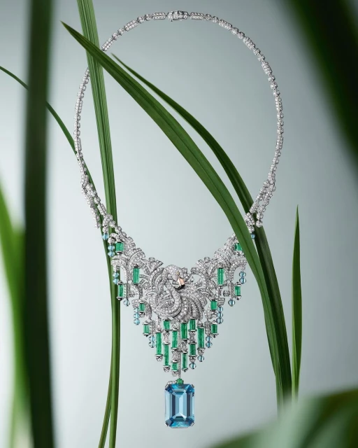 Elegant diamond necklace featuring green and blue gemstones, displayed against a background of vibrant green foliage. Jewelry glamour shot.