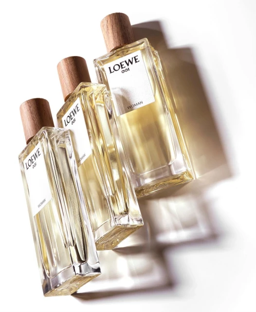 Three Loewe 001 Woman perfume bottles are angled on a white surface casting shadows, product shot, beauty and fashion concept.