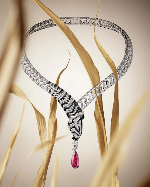 Elegant snake necklace with gemstones displayed against soft beige and gold foliage for a luxury jewelry advertisement.