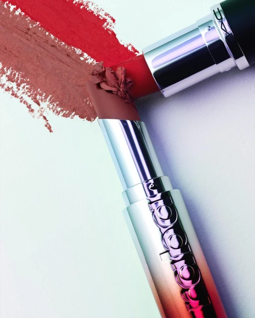 Two lipsticks in shades of red and nude are displayed on a white surface with corresponding color swatches, showcasing beauty products.