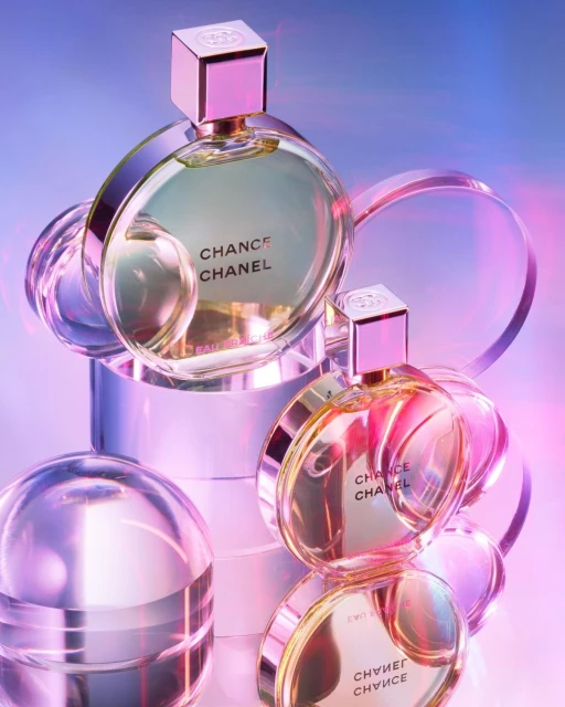Two bottles of Chanel Chance perfume are displayed on clear geometric platforms with a pink and blue background. Beauty and fragrance.