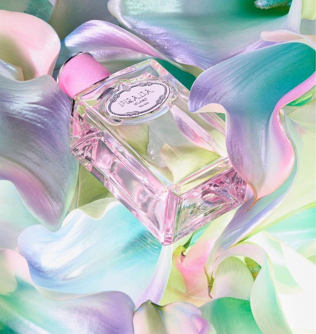 A prism-like Prada perfume bottle sits nestled amongst iridescent lily petals, refracting light and color in a beauty product shot.
