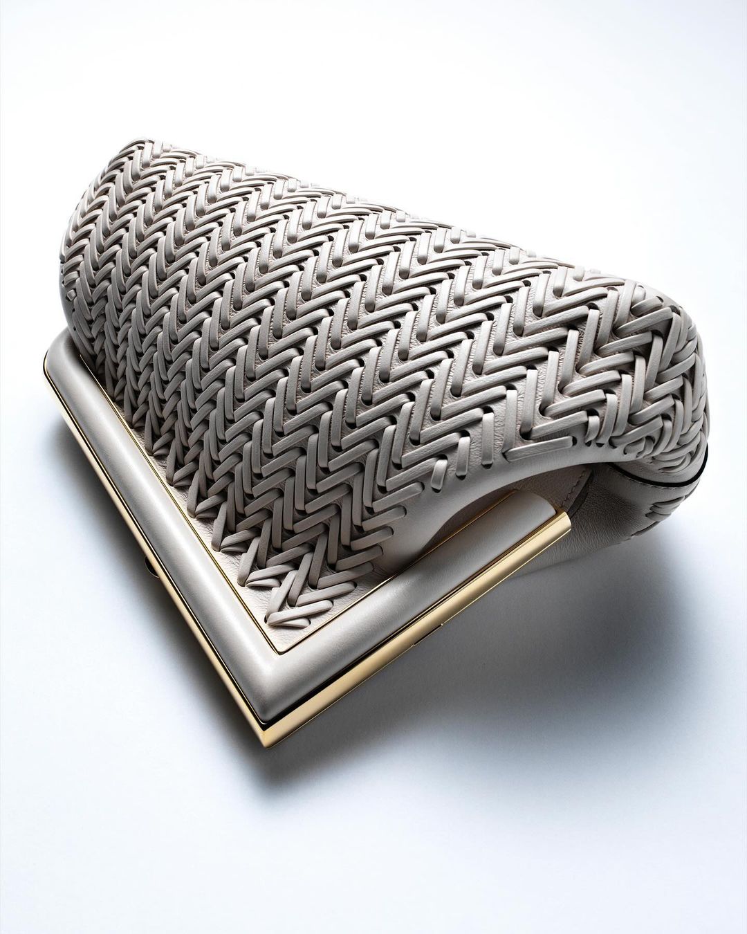 Beige woven clutch purse with gold-toned trim on white backdrop, product shot for fashion accessory, promoting luxury and style.