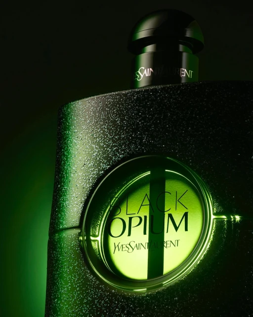Close-up of a Black Opium Yves Saint Laurent perfume bottle against a dark background with green lighting that highlights the brand logo.