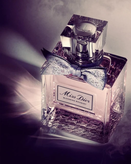 Crystal bottle of Miss Dior Blooming Bouquet perfume with a silver bow sits on a patterned surface with smoke and dramatic lighting.