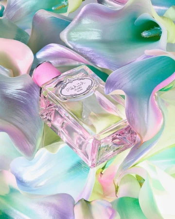 Prada fragrance bottle is surrounded by iridescent calla lily flowers in a studio shot emphasizing beauty and luxury.