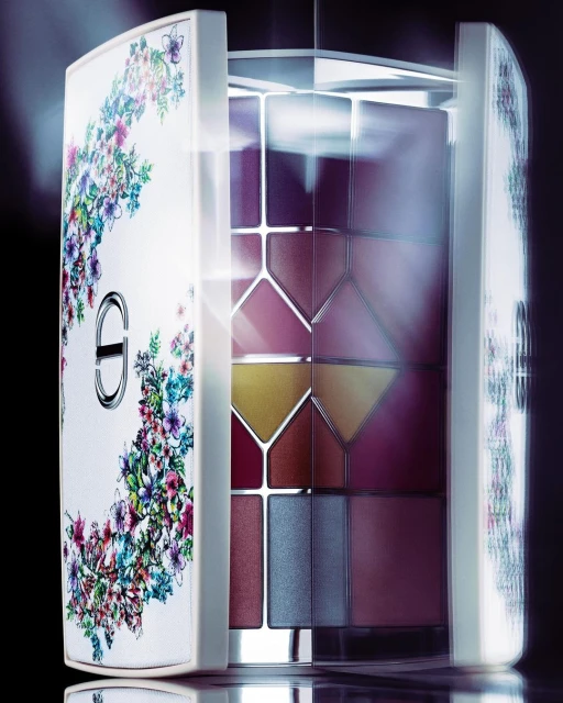 Eye shadow palette in a white floral patterned case. Cosmetics in pink, brown, gold, and blue tones in geometric shapes.