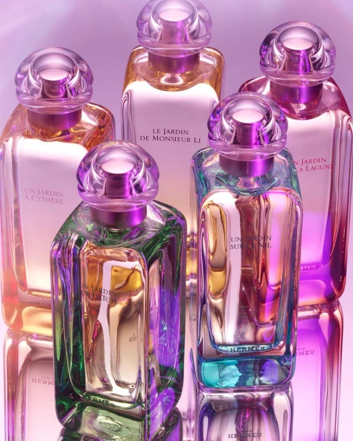 Group of glass perfume bottles with colorful liquid on a reflective surface against a purple background. Features clean product photography.