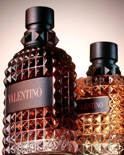Two Valentino perfume bottles with studded design and black caps. The one in front is darker and the other has an amber tone.