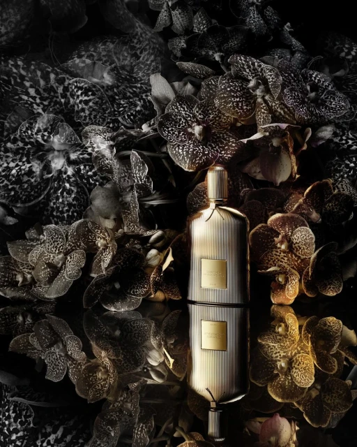 A bottle of perfume is reflected on a glossy surface, surrounded by orchids in various shades of brown and black in a studio setting.