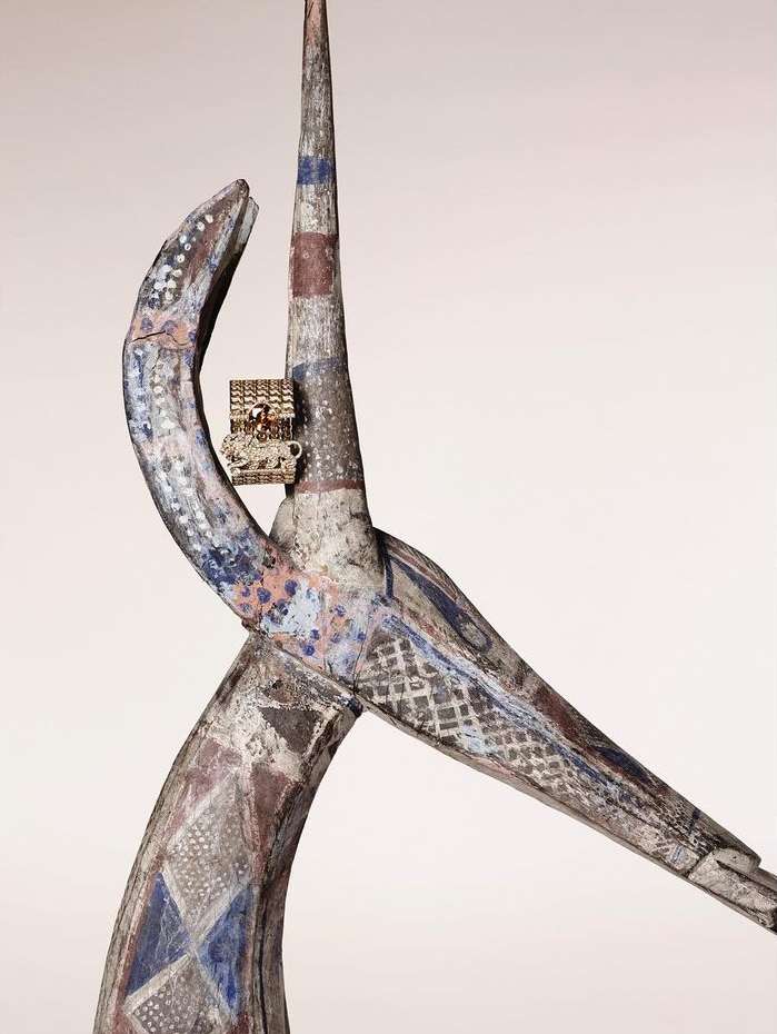 Painted wood carving with patterns, textures, and a miniature structure fixed to the piece, displayed against a plain background.