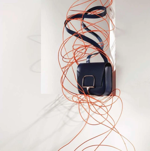 Navy blue leather crossbody bag with silver hardware, adorned with orange string, set against a clean, minimalist white background.