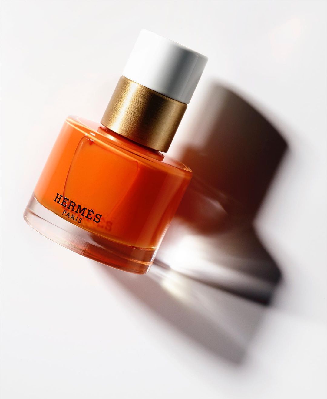 Hermès Paris orange nail polish bottle with white cap and gold accent on a white background, showcasing luxury beauty product.