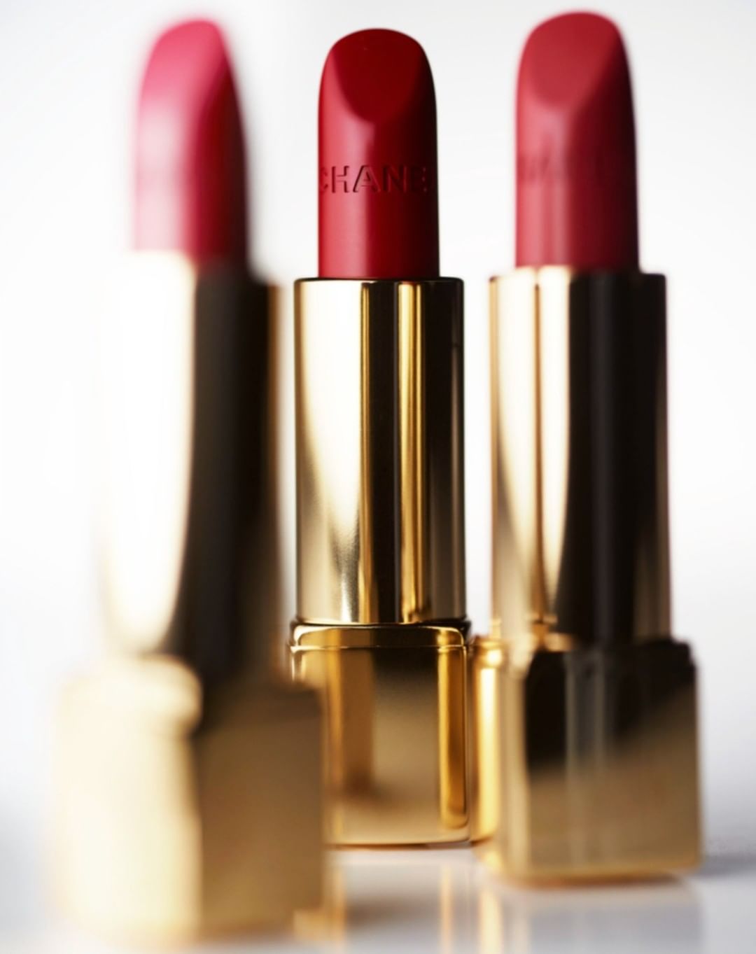 Three red lipsticks with gold tubes are arranged closely together in a beauty or fashion product shot against a white background.