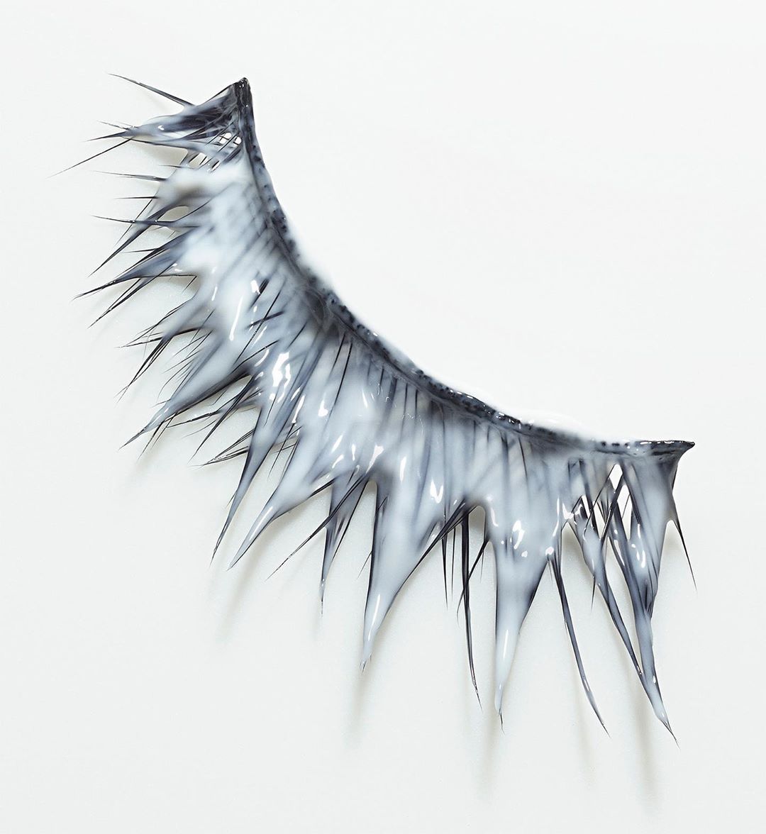 Extreme close-up of a false eyelash with white cream applied. The lash curves, with spikes covered in white, on a clean white background.