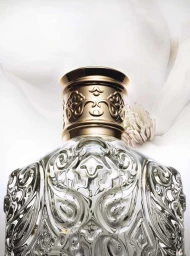 Close-up of an ornate glass perfume bottle with an intricate metal cap and white fabric backdrop