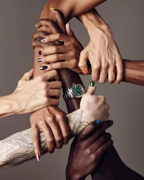 Close-up of interlocked arms and hands of diverse people with colorful manicures and a silver wristwatch against a grey background.