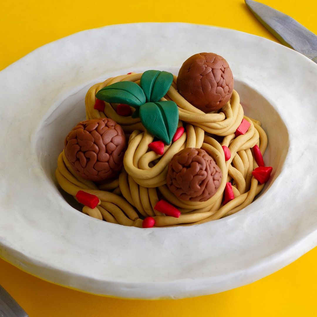 Close-up of a plate of spaghetti and meatballs with basil leaves on a yellow background, showcasing food photography with studio lighting.
