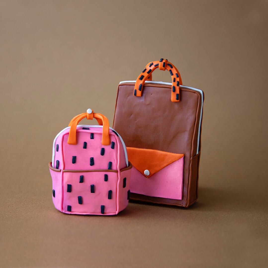 Two artistically crafted bags, a pink patterned backpack and a brown tote, set against a neutral backdrop showcasing unique design.