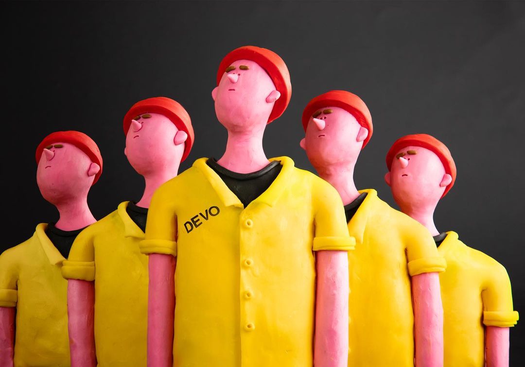 Five clay figures stand in a row wearing yellow shirts and red hats against a dark background in a stylized animation.
