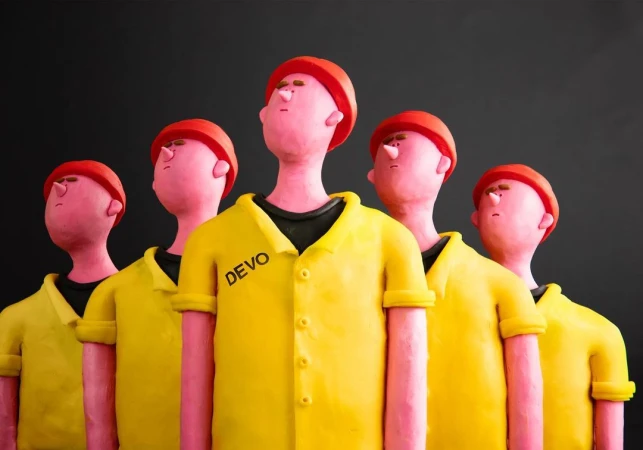 Five clay figures stand in a row wearing yellow shirts and red hats against a dark background in a stylized animation.