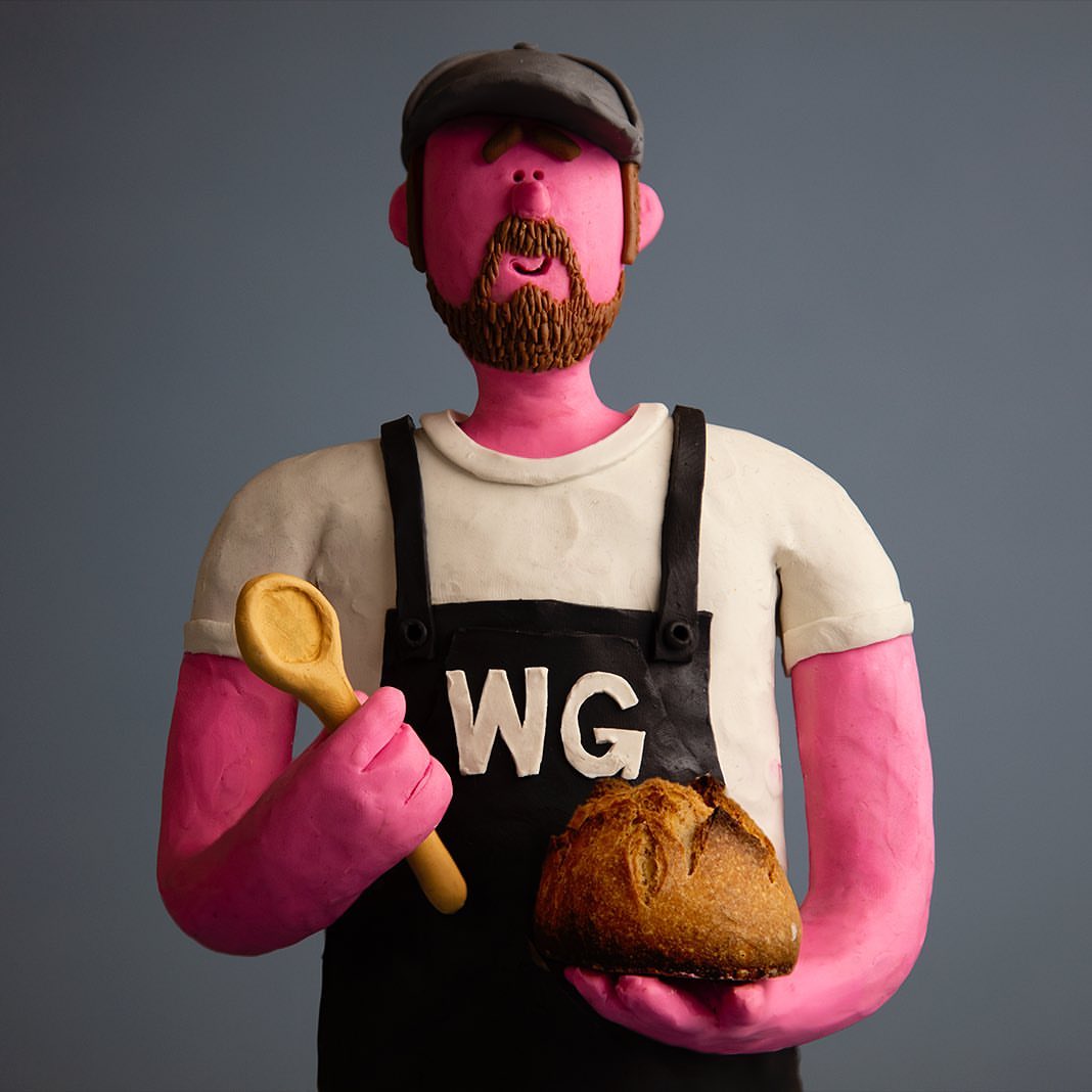 Claymation-style baker figure in apron holding bread loaf and wooden spoon, captured against a neutral backdrop.