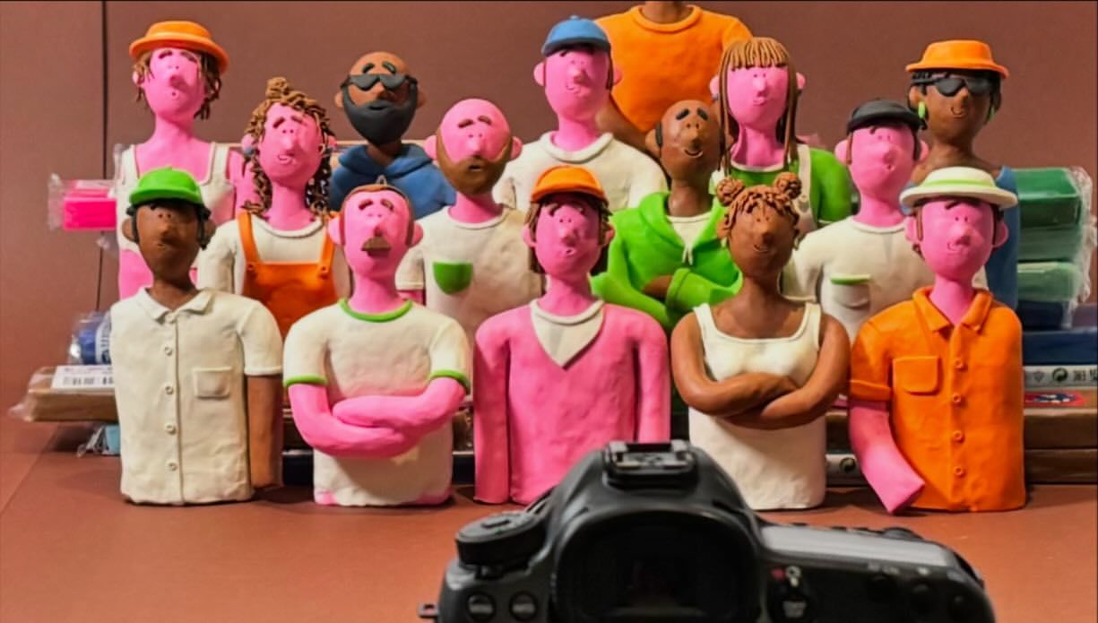 Stop-motion animation featuring a diverse group of figures in colorful attire, standing together and facing the camera in a studio setting.