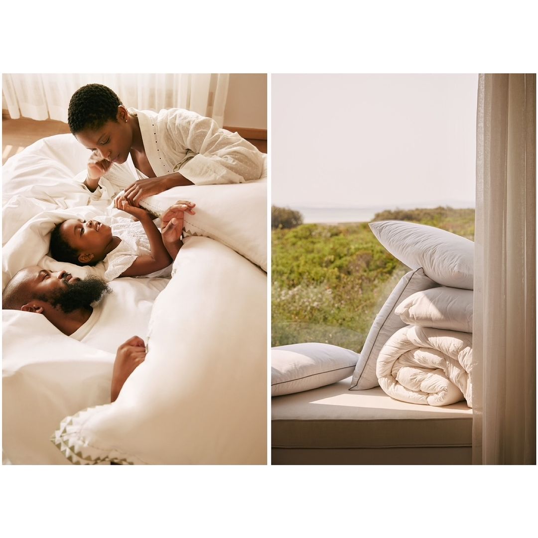 Cozy scene in a bedroom featuring an adult female and a child in bed alongside a window view of lush greenery and a stack of pillows.