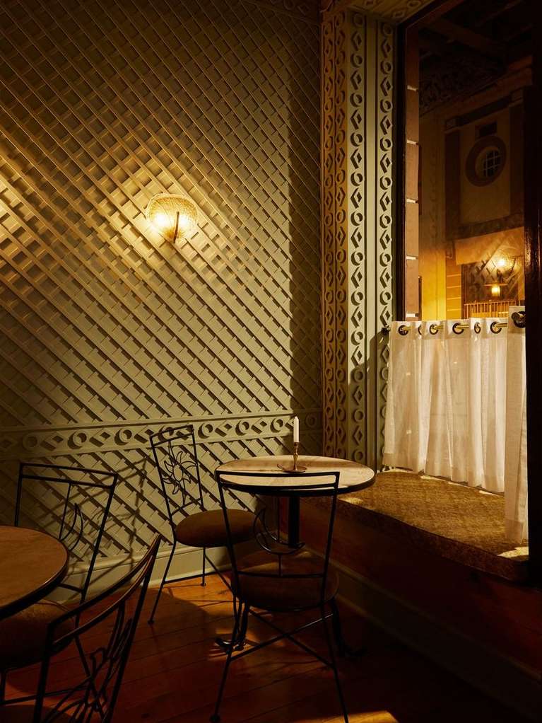 Indoor cafe scene features round tables and wrought iron chairs, illuminated by wall sconces, creating a warm, inviting ambiance.