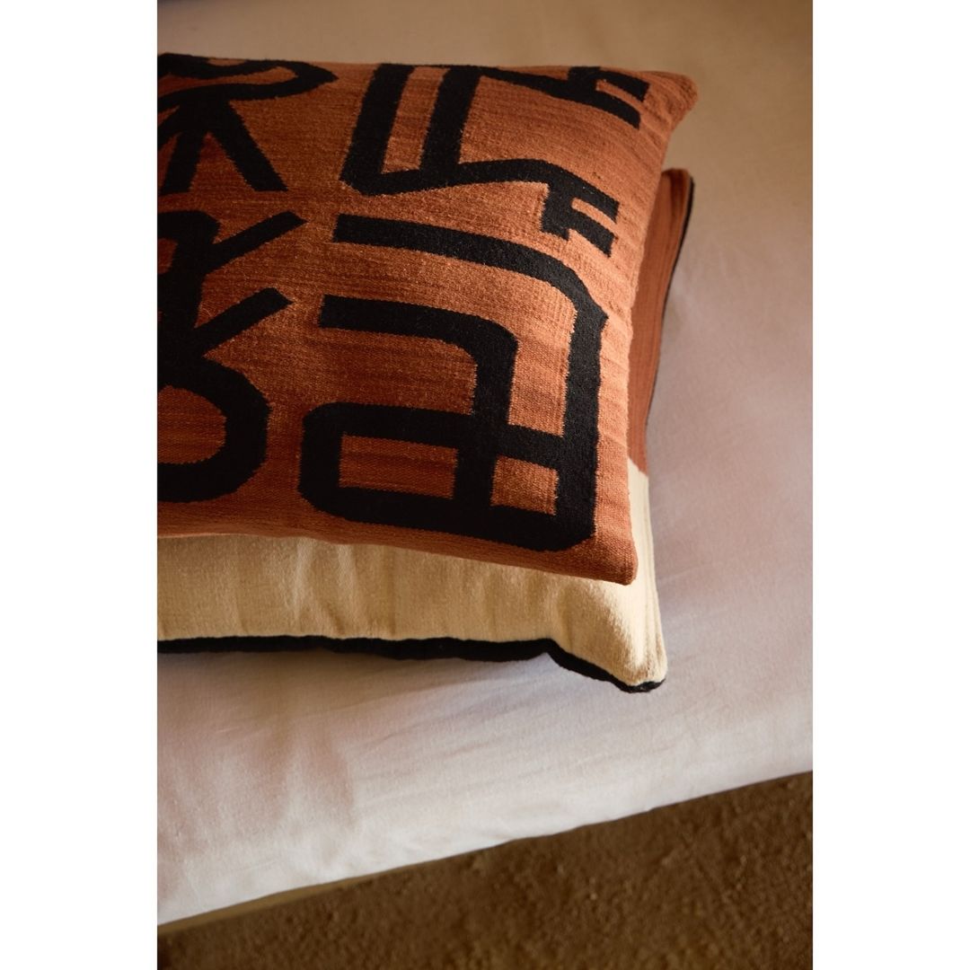 Close-up of a decorative throw pillow with abstract black geometric shapes against a textured brown and beige background.
