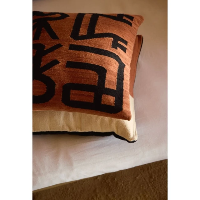 Close-up of a decorative throw pillow with abstract black geometric shapes against a textured brown and beige background.
