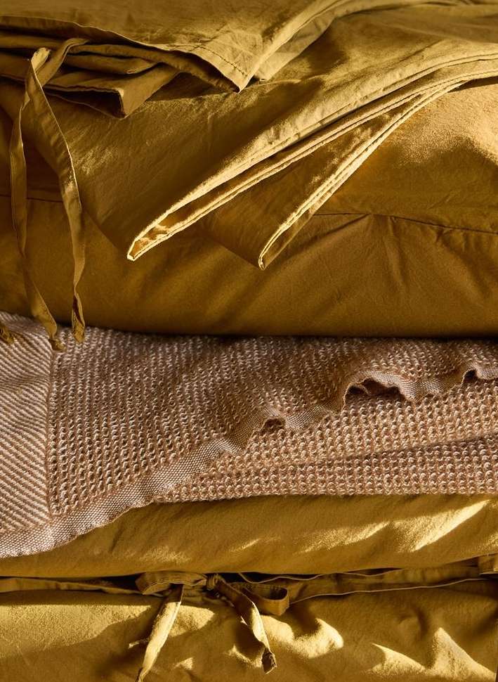 Close-up of neatly stacked golden-yellow fabric and waffle-weave blanket, showcasing texture and color in a warm, inviting indoor scene.