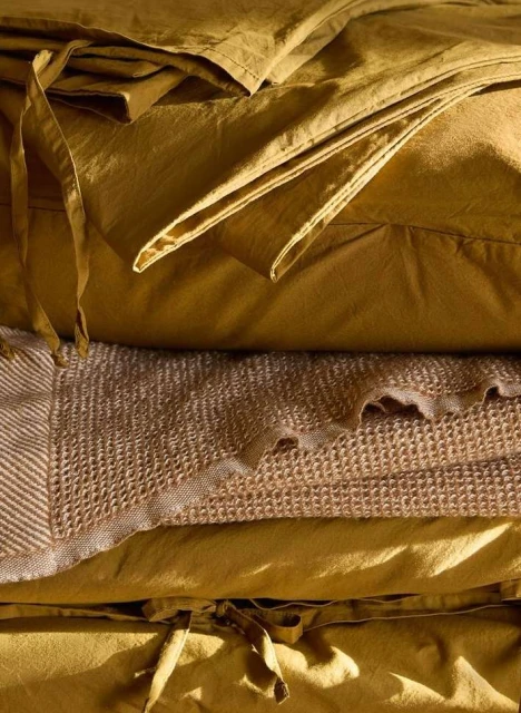 Close-up of neatly stacked golden-yellow fabric and waffle-weave blanket, showcasing texture and color in a warm, inviting indoor scene.