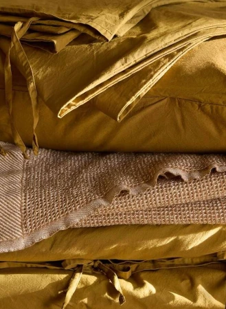 Close-up of neatly stacked golden-yellow fabric and waffle-weave blanket, showcasing texture and color in a warm, inviting indoor scene.