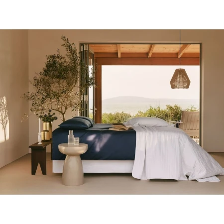 Serene interior showcases a styled bed with blue sheets and white quilt, complemented by natural light and decorative elements in a minimalist setting.