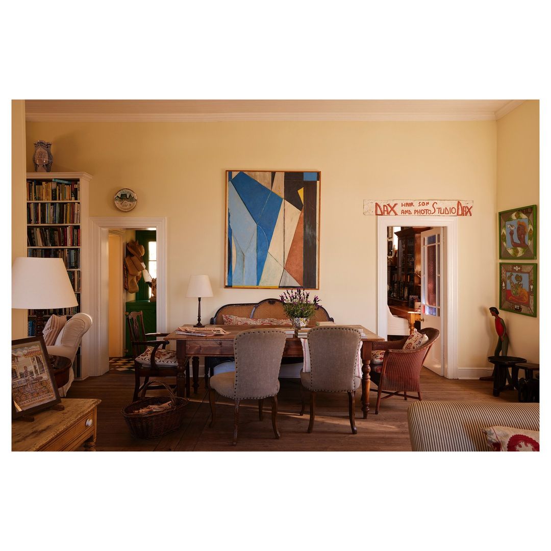 Interior of a living room featuring a dining table set with chairs, an abstract painting, and decorative elements in soft, natural light.