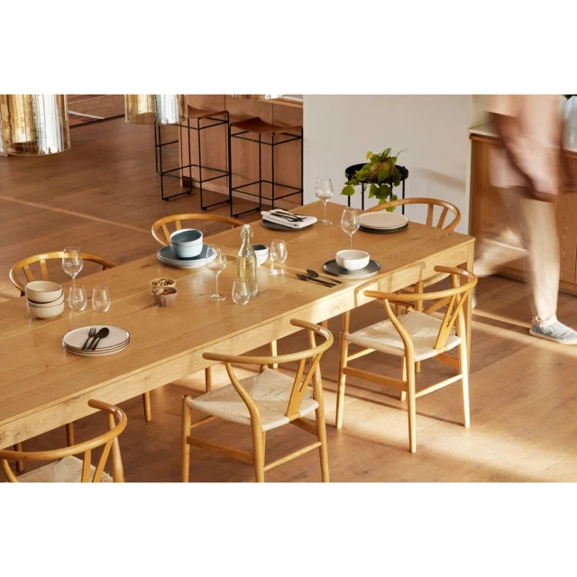 Dining room featuring a light wood table set with tableware and glasses, surrounded by light wood chairs with woven seats.