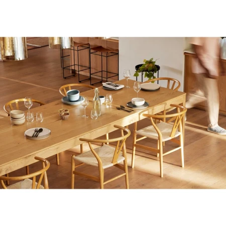 Dining room featuring a light wood table set with tableware and glasses, surrounded by light wood chairs with woven seats.