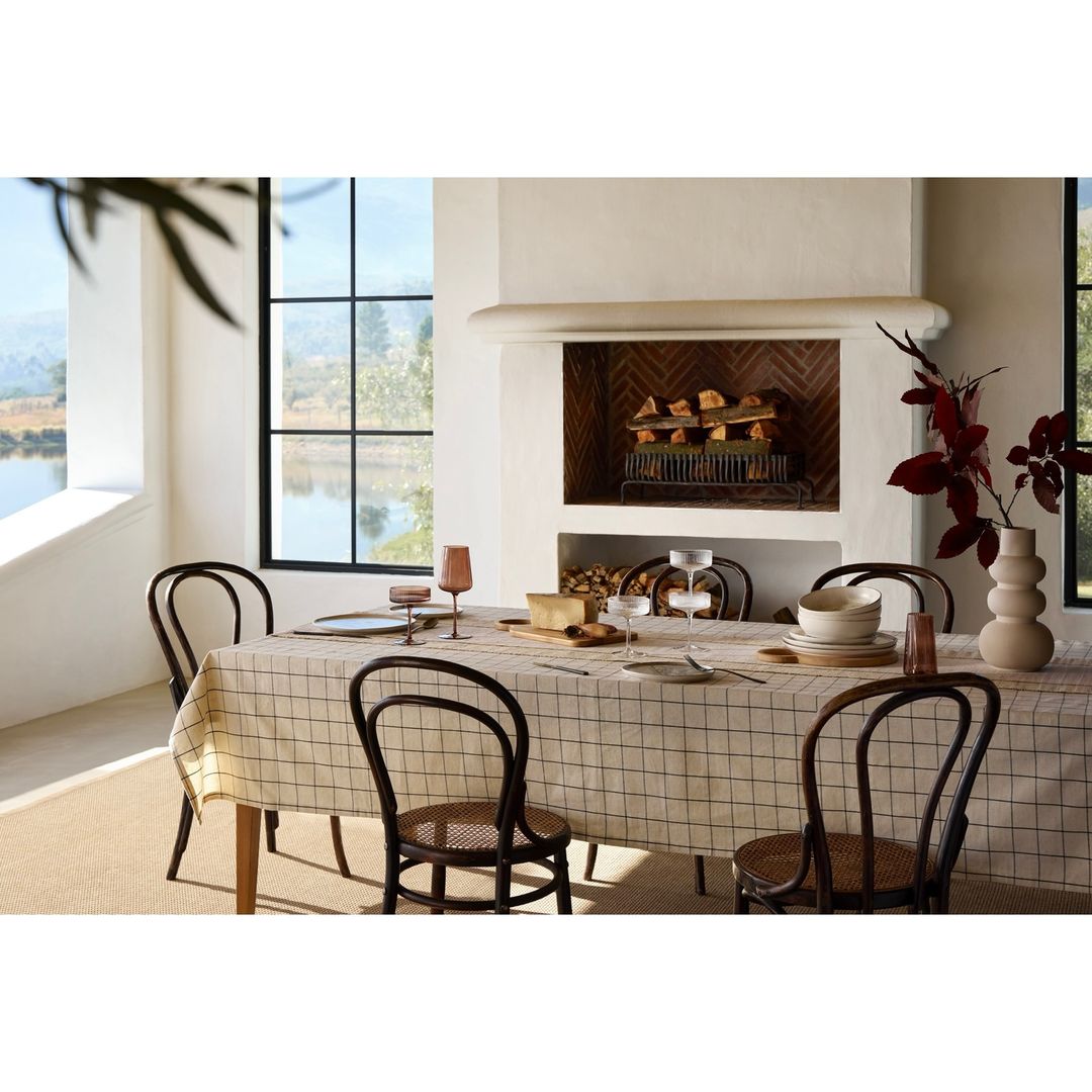 Dining room interior featuring a table set for a meal with plates, glasses, cutlery, and a vase, next to a fireplace.